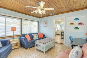 A living room with a ceiling fan, a blue sofa, a wooden coffee table, and a dining area with a table and chairs. - Lovely St Pete Beach Cottage, Walk to Beach & Town (Gulfport)