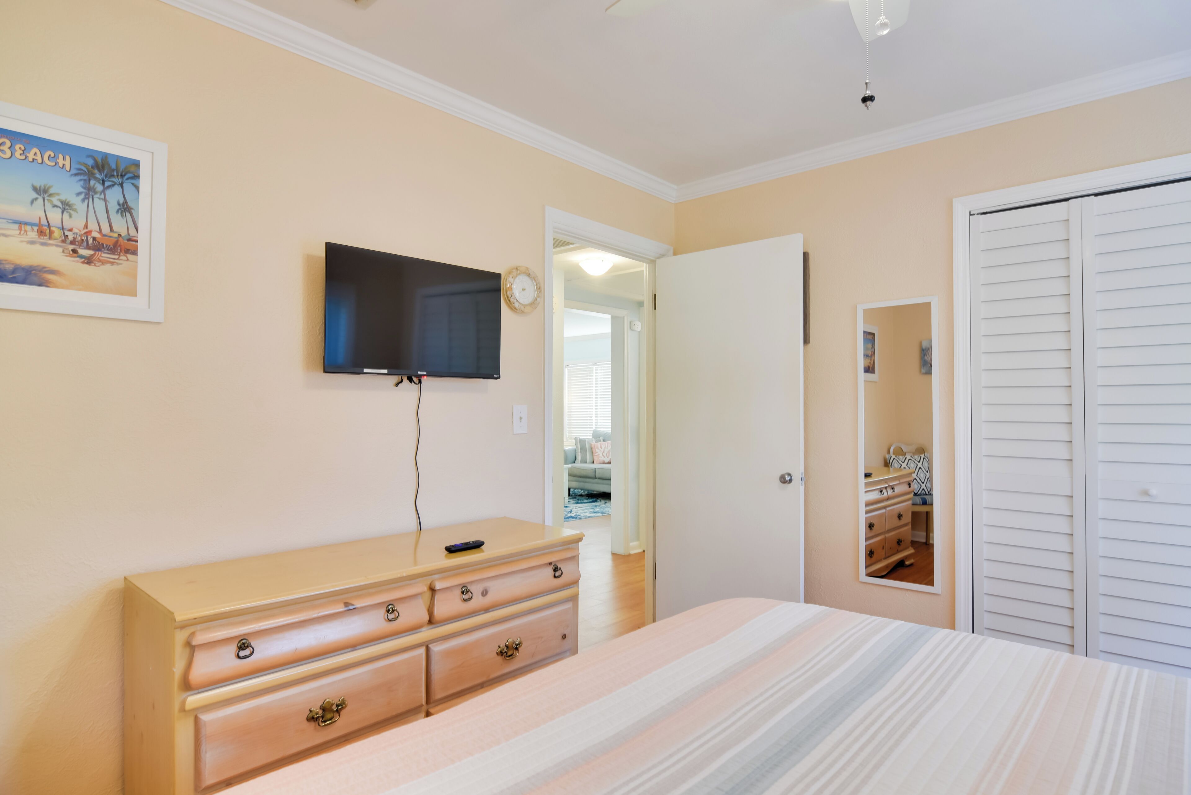 Un dormitorio con cama, cómoda, televisor montado en la pared y armario.