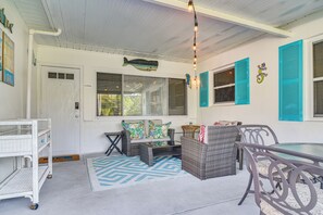 A covered porch with wicker furniture, a dining table, and a ceiling light fixture. - Lovely St Pete Beach Cottage, Walk to Beach & Town (Gulfport)