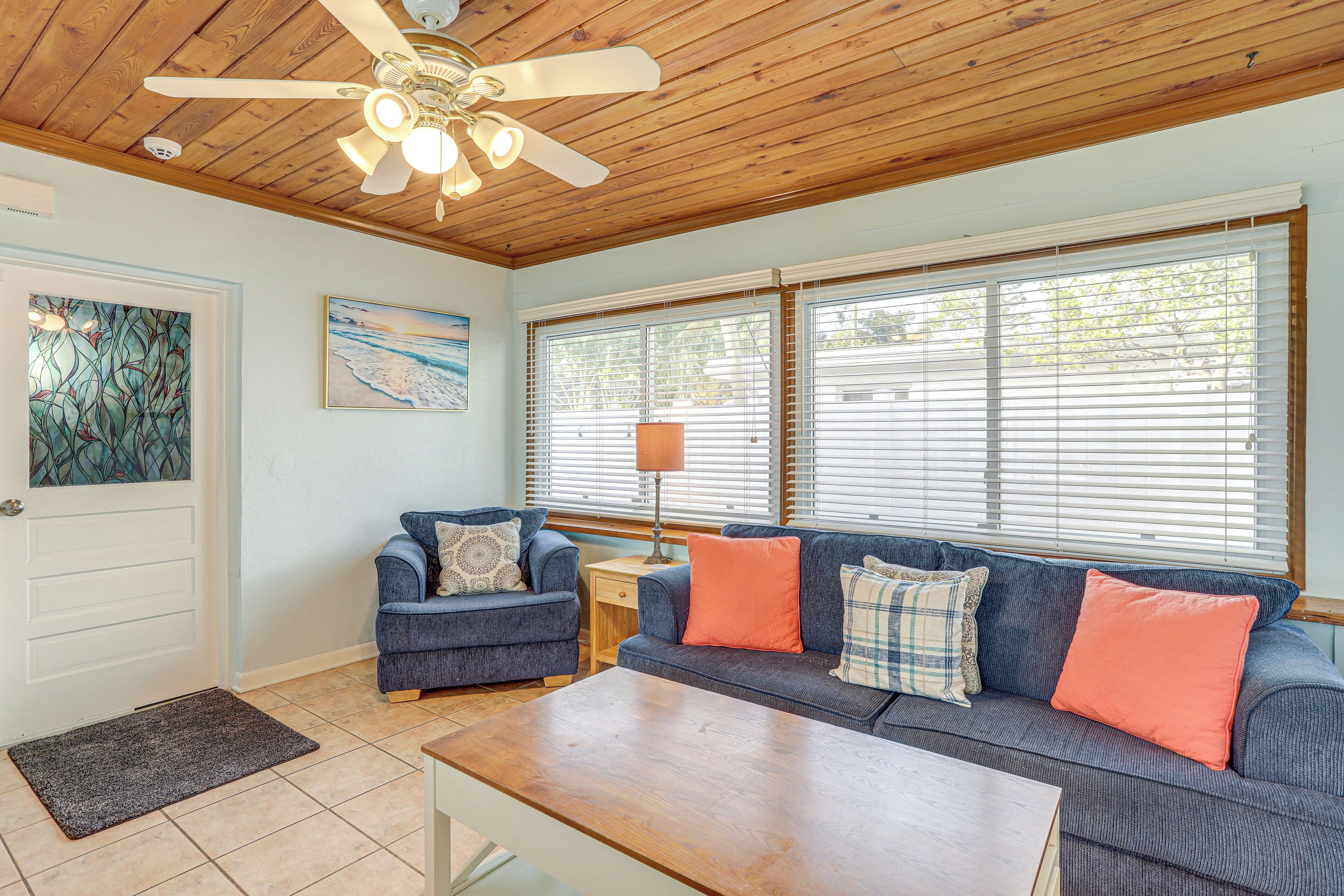 A living room with a ceiling fan, a sofa set, a coffee table, and a door with a doormat.