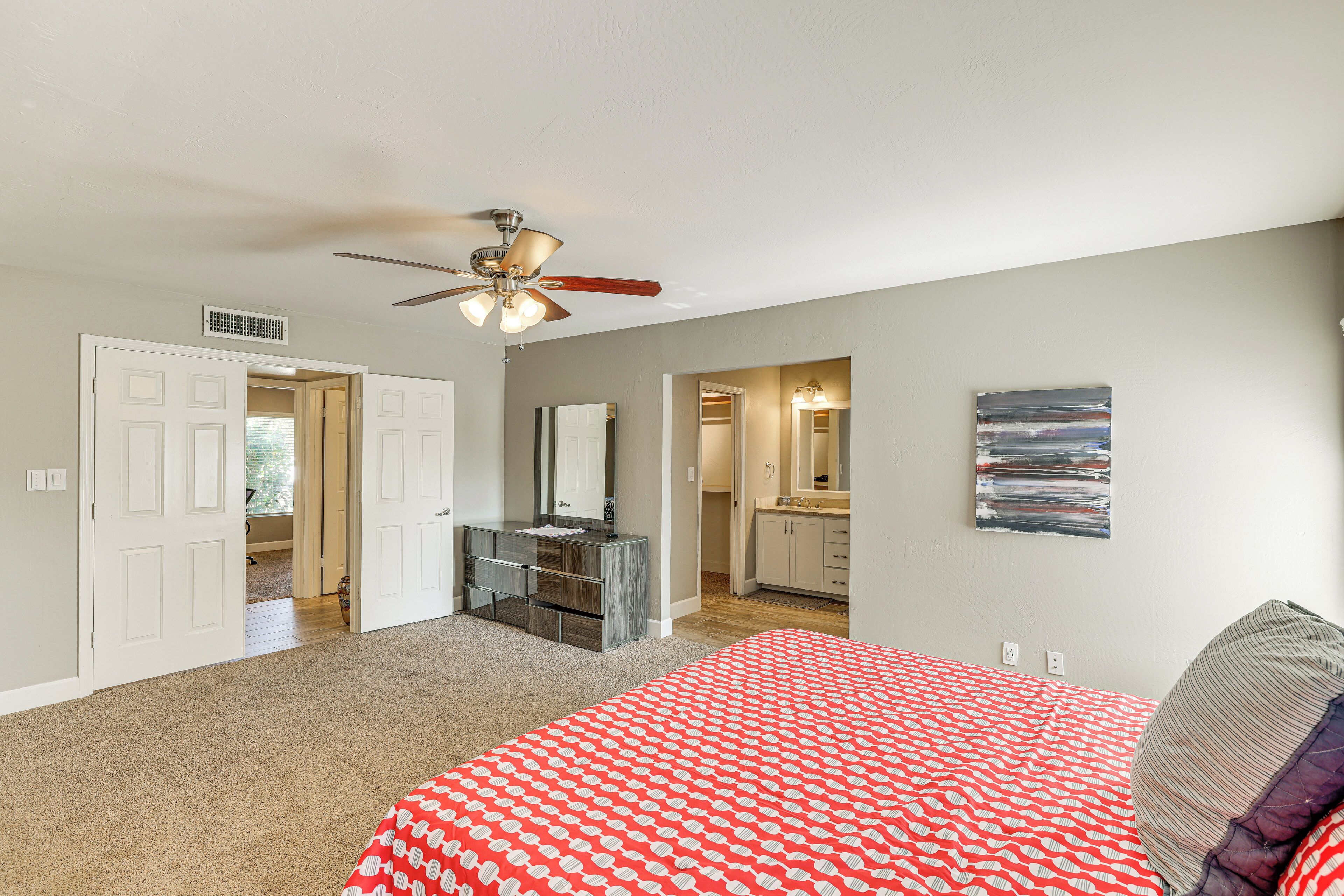 A bedroom with a bed, a ceiling fan, a dresser, and a bathroom visible through an open door.
