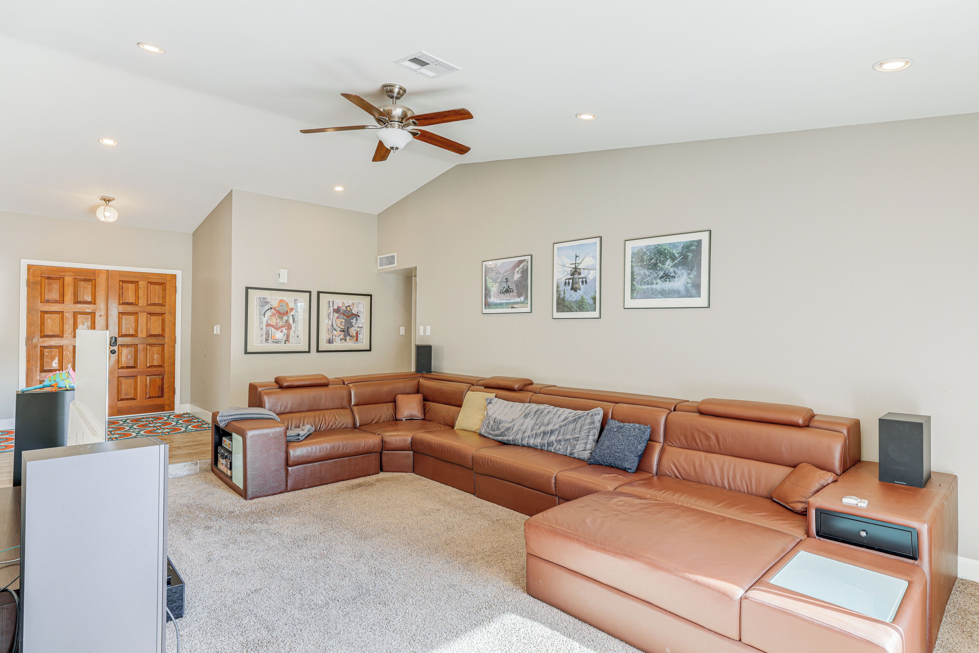 A spacious living room with a large L-shaped sectional sofa, a ceiling fan, and framed pictures on the wall.
