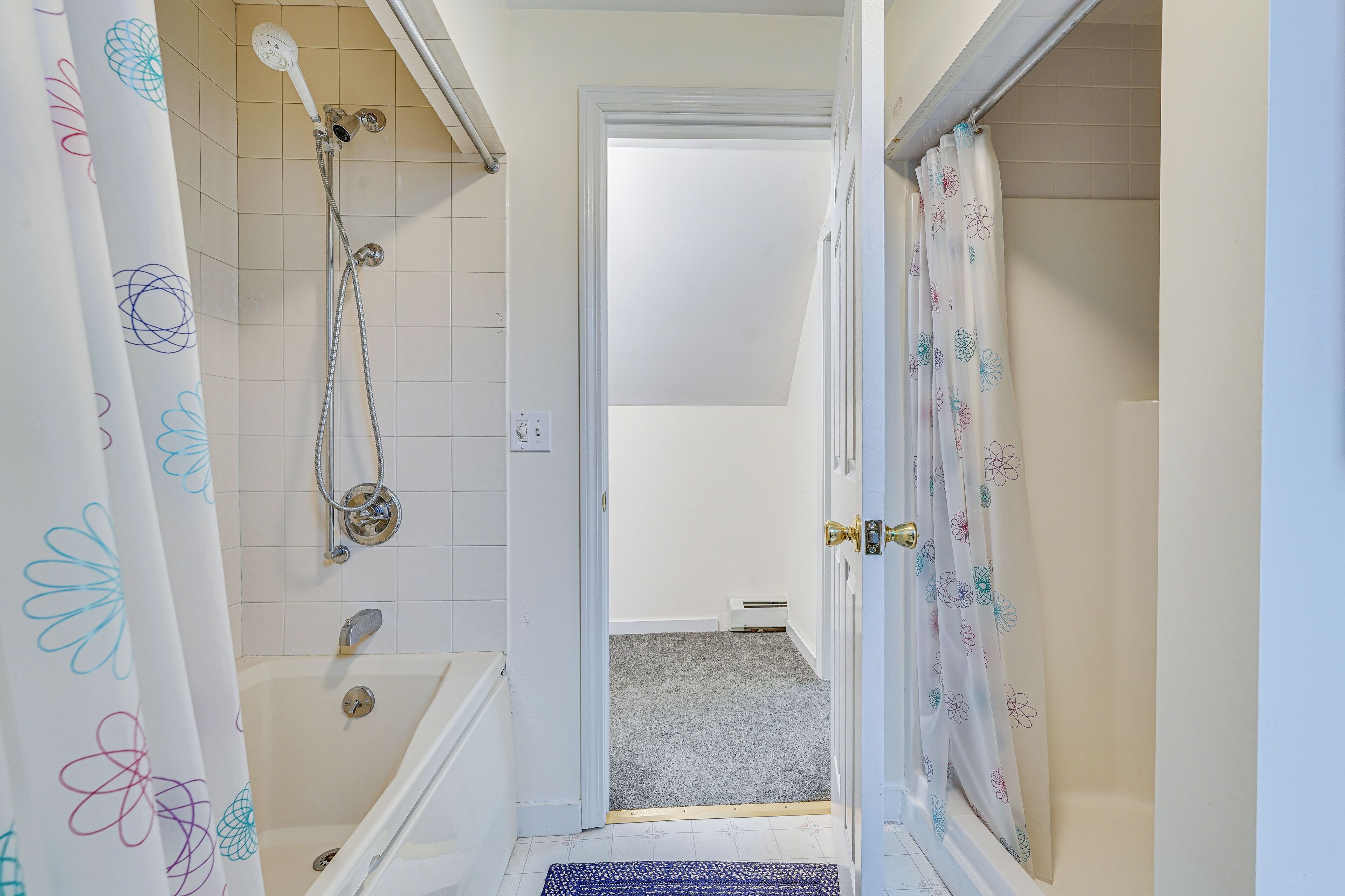 A narrow bathroom with a bathtub, shower, and toilet.
