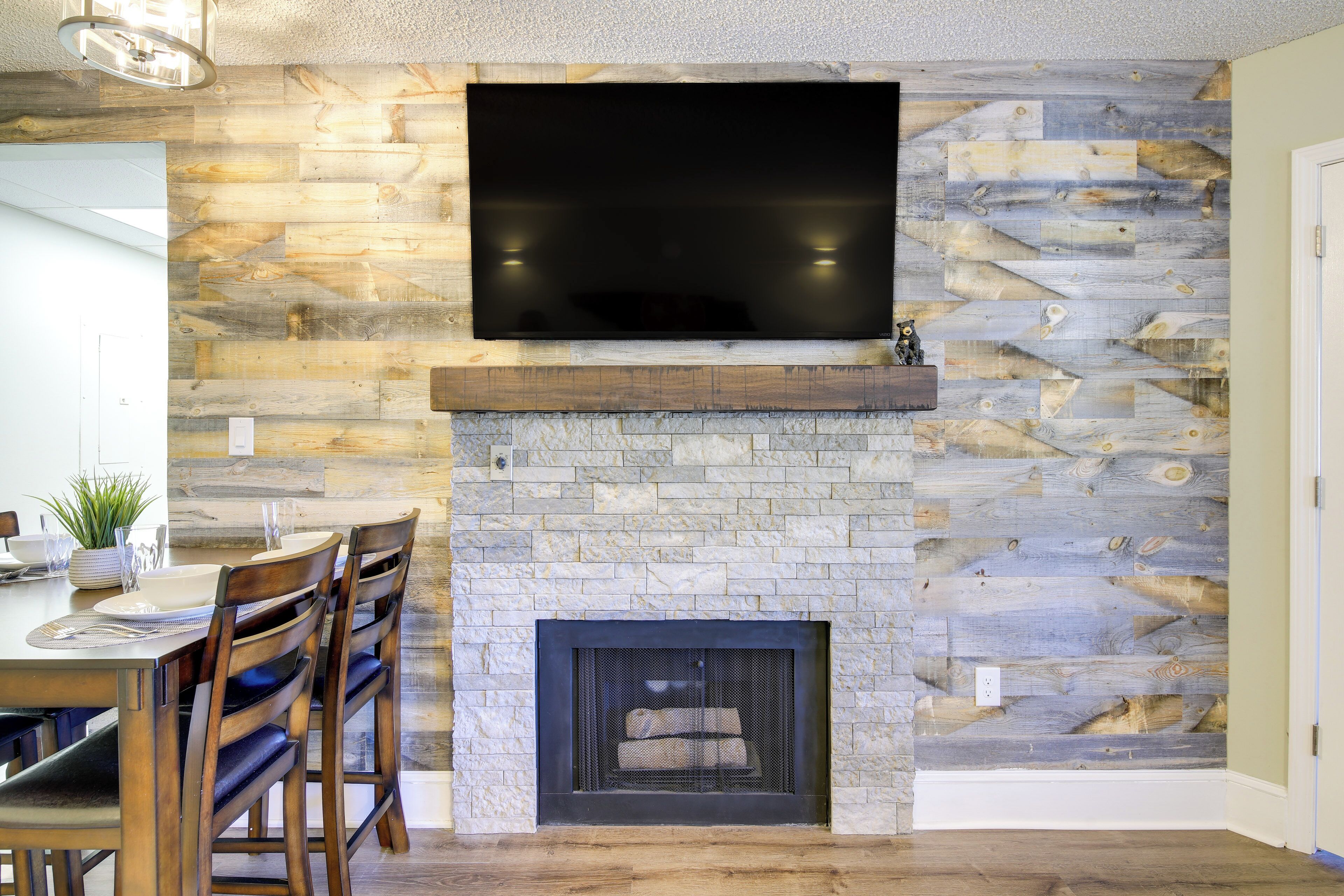Una sala de estar moderna con una chimenea de piedra, un televisor de pantalla plana montado encima y un comedor con sillas de madera y una mesa.