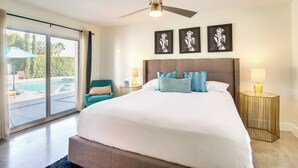 Een ruime slaapkamer met een groot bed, een plafondventilator en uitzicht op een zwembad door een schuifdeur.