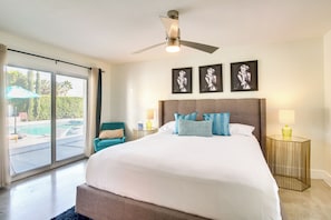 Een ruime slaapkamer met een groot bed, een plafondventilator en uitzicht op een zwembad door een schuifdeur.