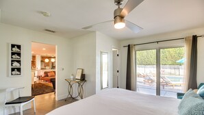 Een ruime slaapkamer met een groot bed, een plafondventilator en uitzicht op een buitenzwembad.