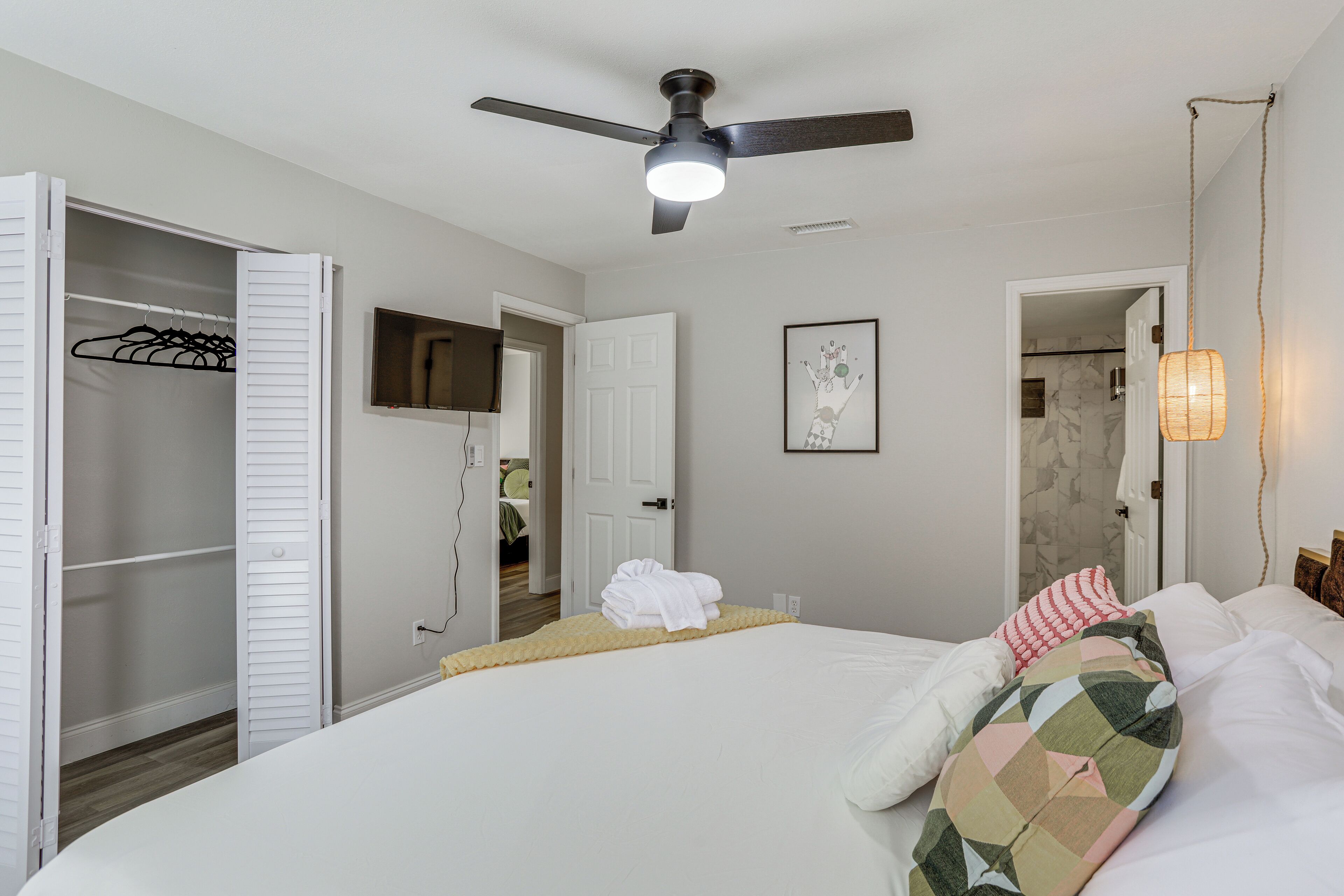 A bedroom with a bed, a ceiling fan, a closet, and a bathroom door.