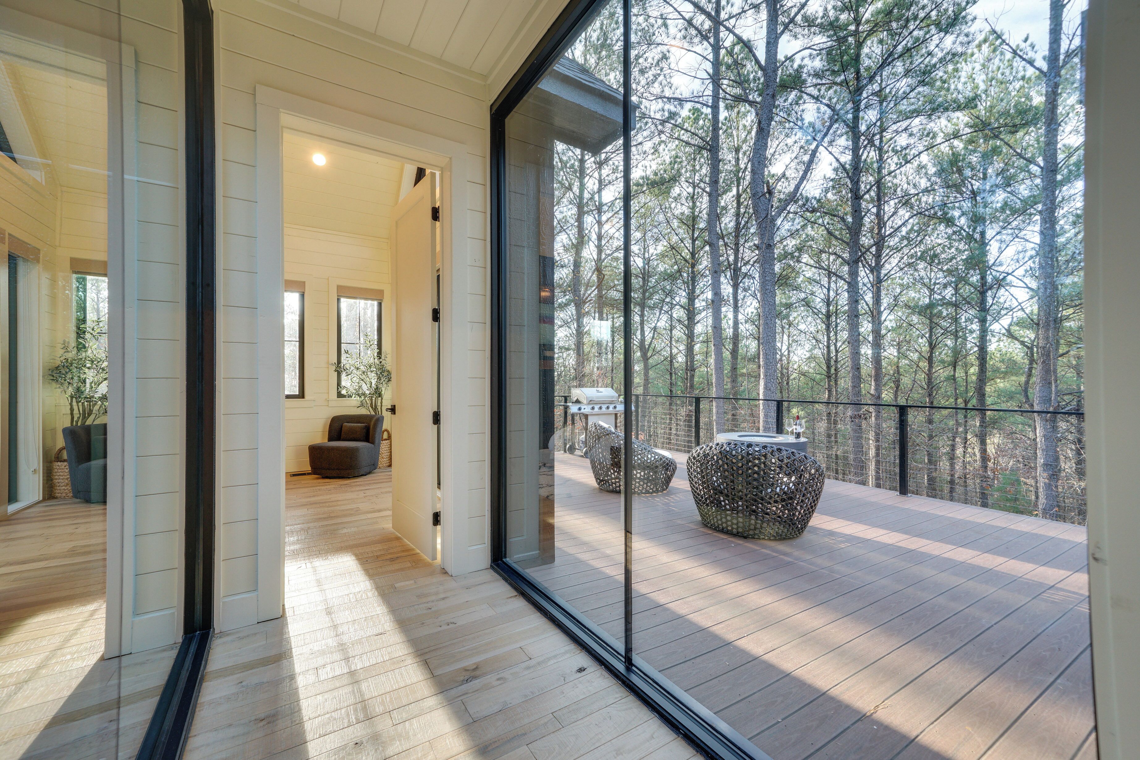 Un interior moderno con piso de madera, puerta de vidrio que da a un balcón con vista a un bosque.