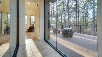 Un interior moderno con piso de madera, puerta de vidrio que da a un balcón con vista a un bosque.