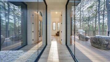 A modern interior with a glass wall leading to a deck, wooden flooring, and a seating area with unique chairs.