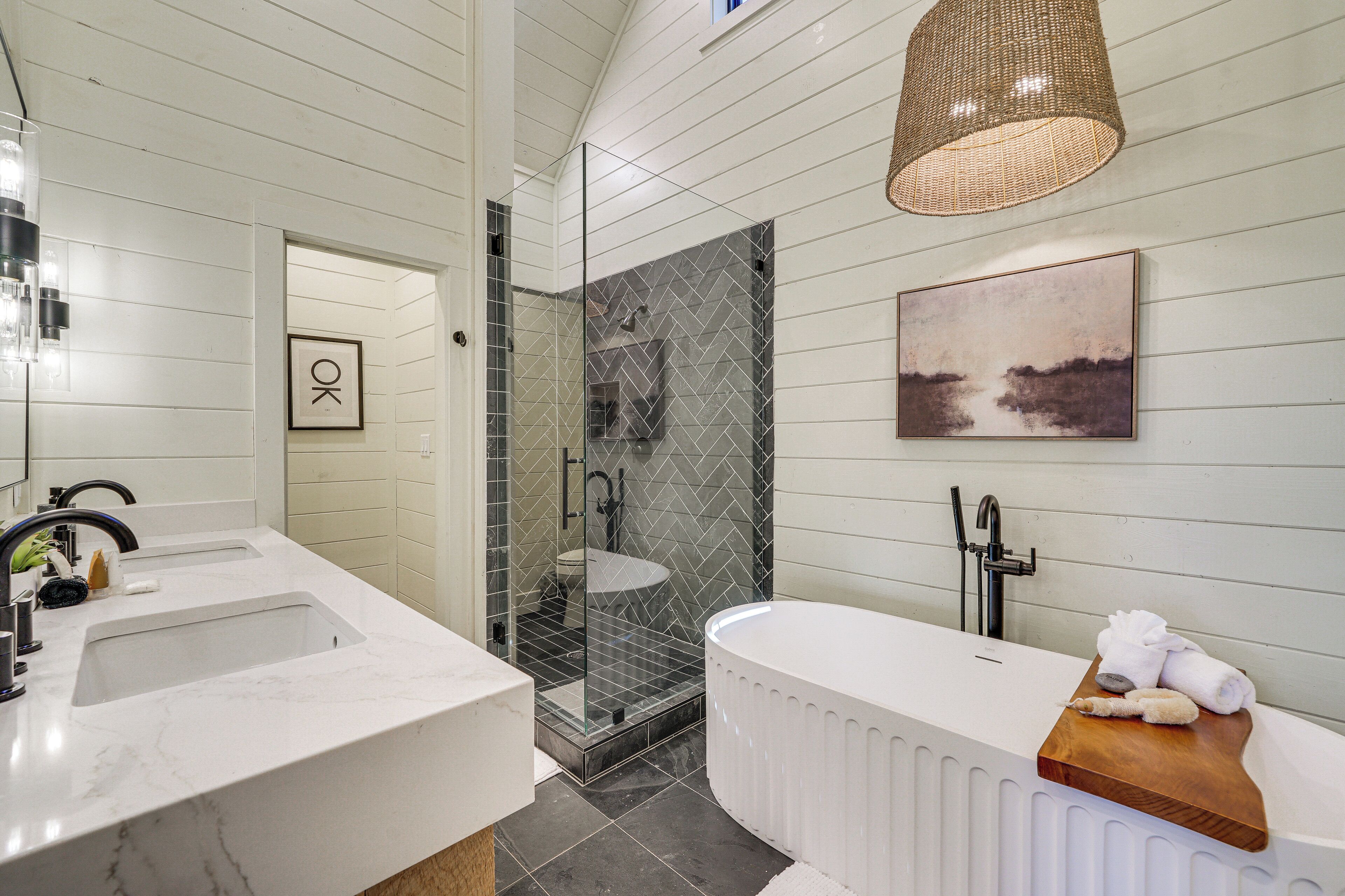 A modern bathroom with a double sink, a glass-enclosed shower, a freestanding bathtub, and a wooden tray with towels.