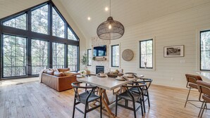 Une salle à manger spacieuse, dotée d’une grande table et de chaises, d’une cheminée en pierre et de grandes fenêtres offrant une vue sur l’extérieur.