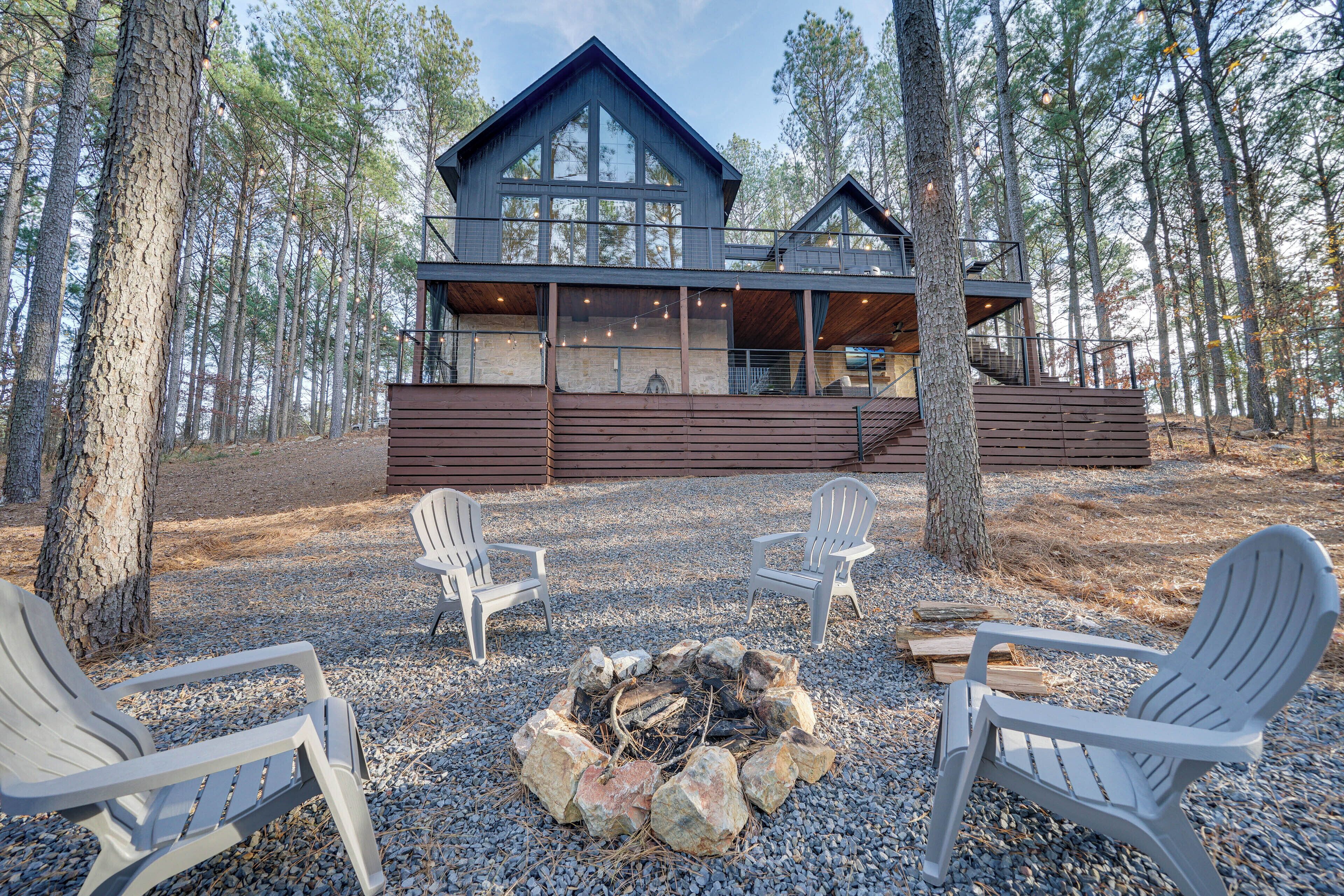 A cabin with a fire pit, two Adirondack chairs, and a view of the surrounding forest.