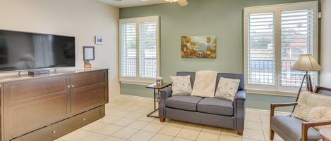A spacious living room with a grey sofa, a wooden coffee table, and a flat-screen TV on a cabinet.