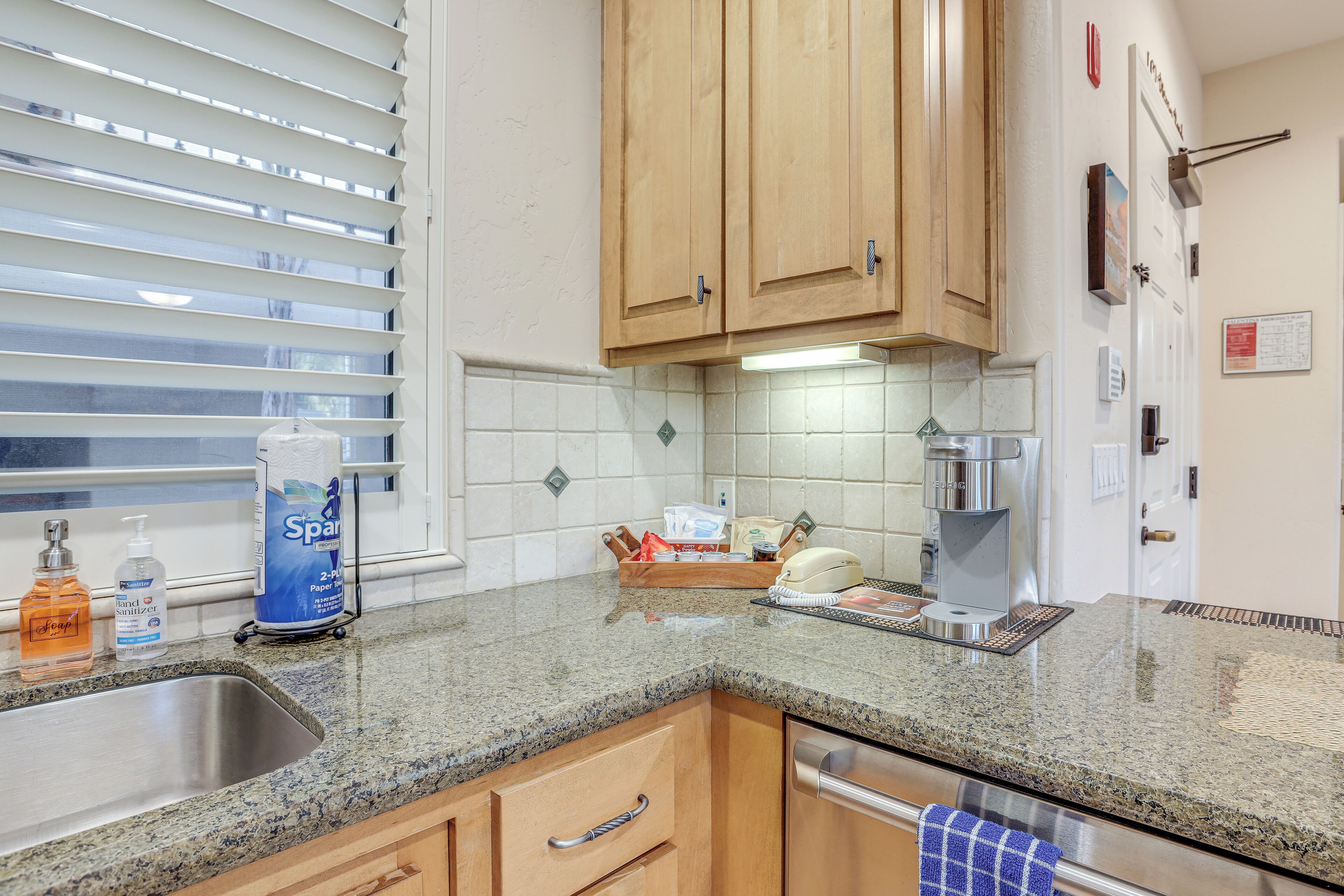 Una cocina con armarios de madera, encimera de granito, pileta de acero inoxidable y cafetera.