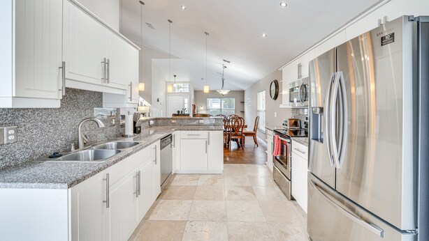 A modern kitchen with white cabinets, granite countertops, stainless steel appliances, and a central island.