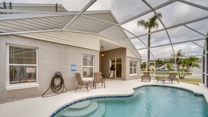 A pool area with a curved edge, outdoor seating, and a covered patio.
