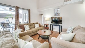 A living room with a sofa, armchairs, a coffee table, a TV, and a dining area with chairs and a table.