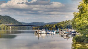 A calm river with boats docked on the right, a bridge in the background, and a forested hillside. - Waterfront Home: Allegheny River Access, Dock Slip (Ford City)