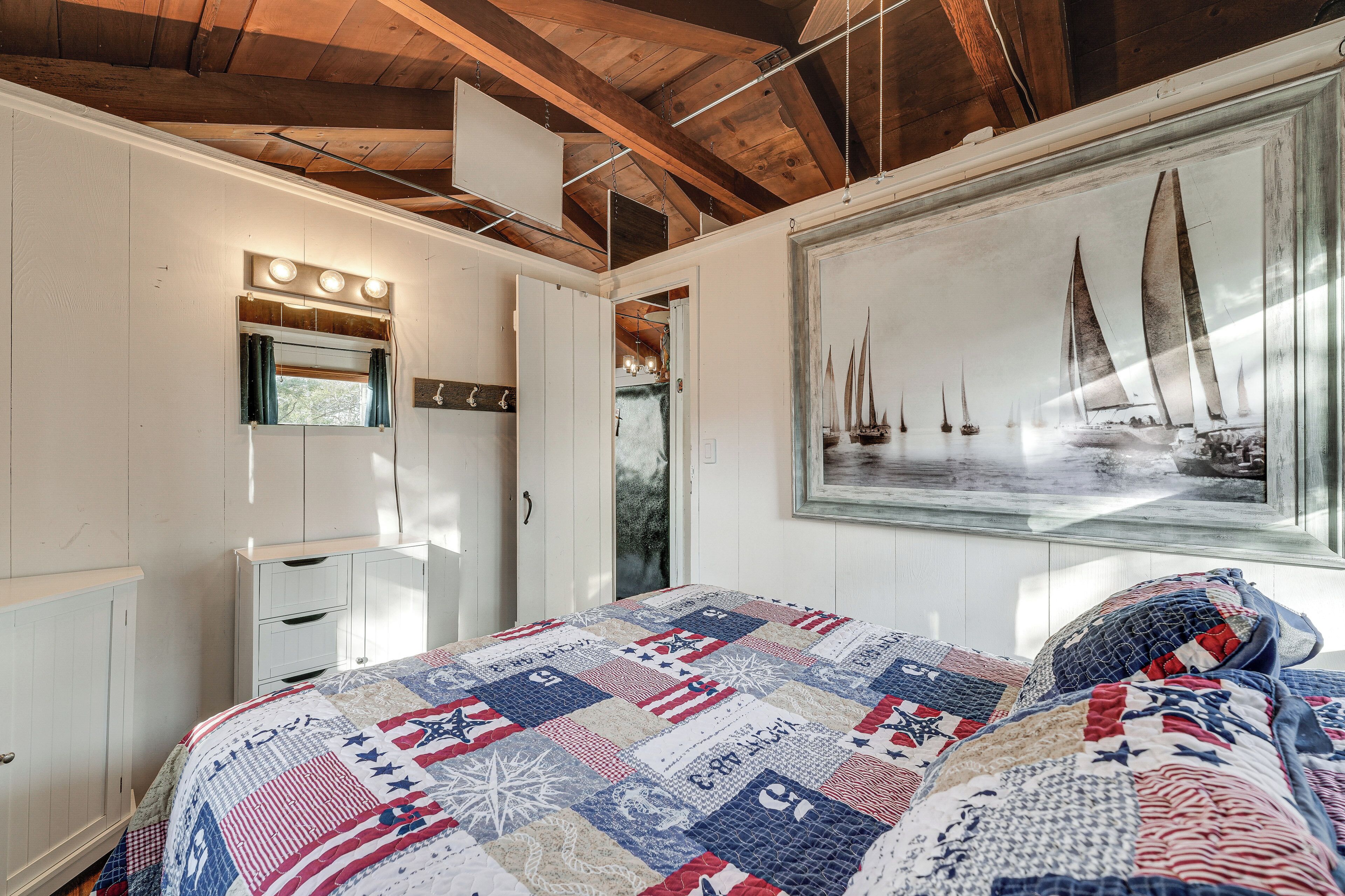 A bedroom with a bed, a dresser, a mirror, and a painting of sailboats.