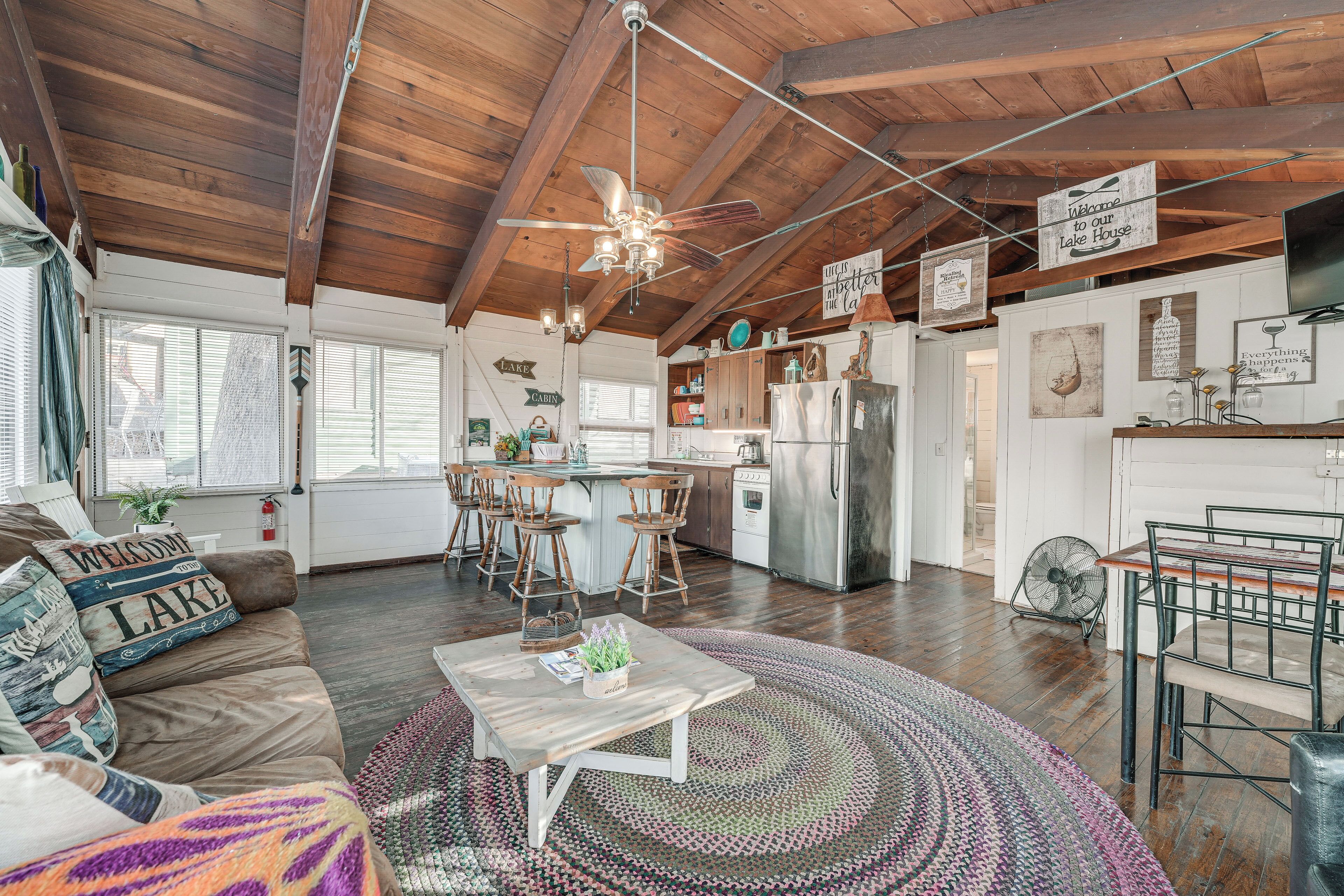 A spacious living area with a wooden ceiling, a central island with seating, a kitchen with modern appliances, and a dining area with metal chairs.
