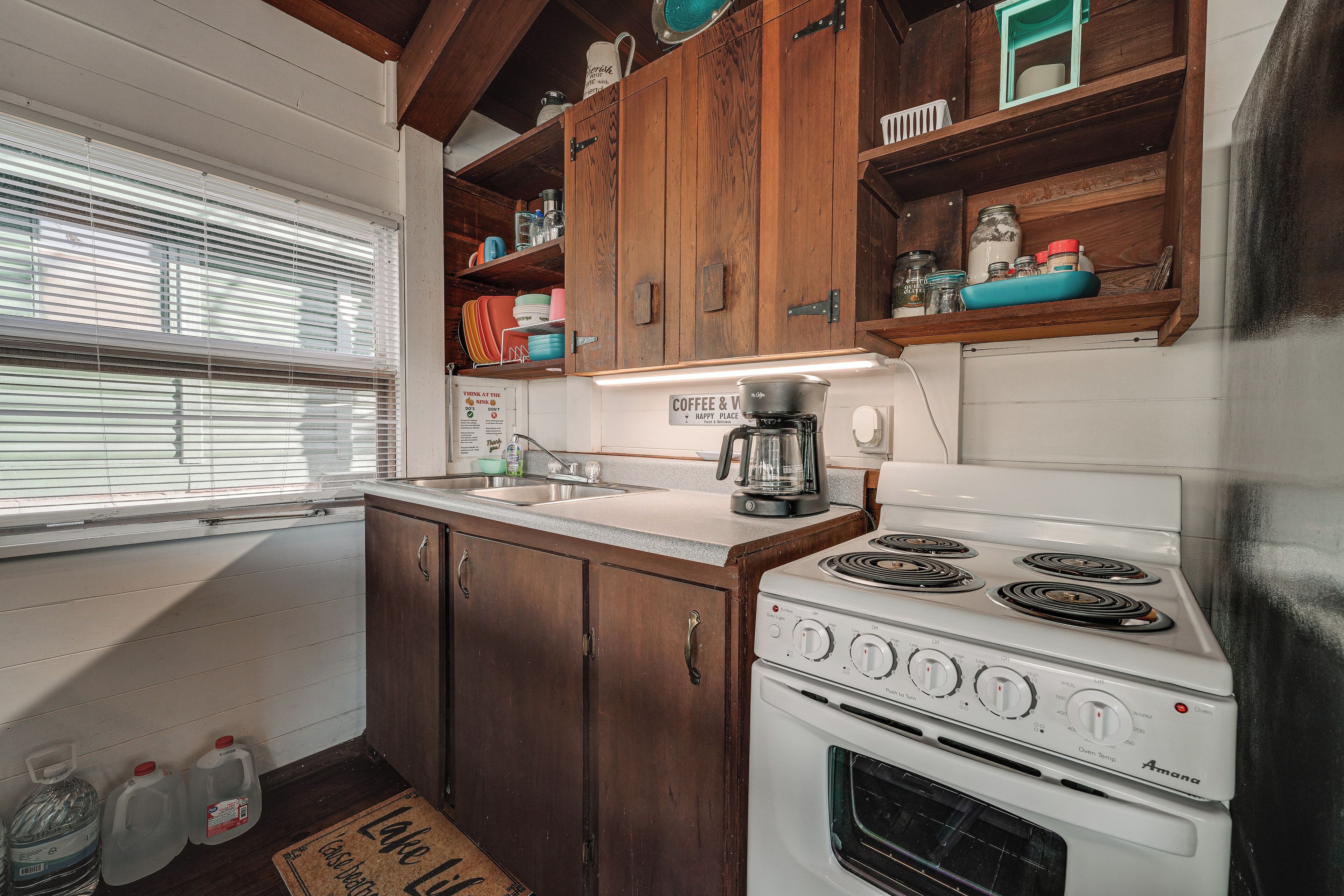 A kitchen with wooden cabinets, a white stove, and a window with blinds.