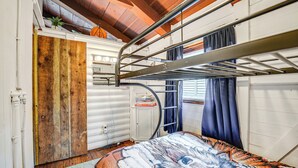 Ein Schlafraum mit Etagenbetten, einer Holztür, einem weißen Schrank und einem Fenster mit Vorhängen.