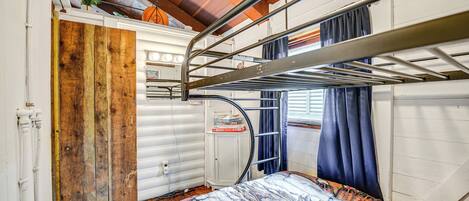 Ein Schlafraum mit Etagenbetten, einer Holztür, einem weißen Schrank und einem Fenster mit Vorhängen.