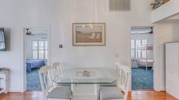 A dining area with a glass-top table, white chairs, and a framed picture on the wall.