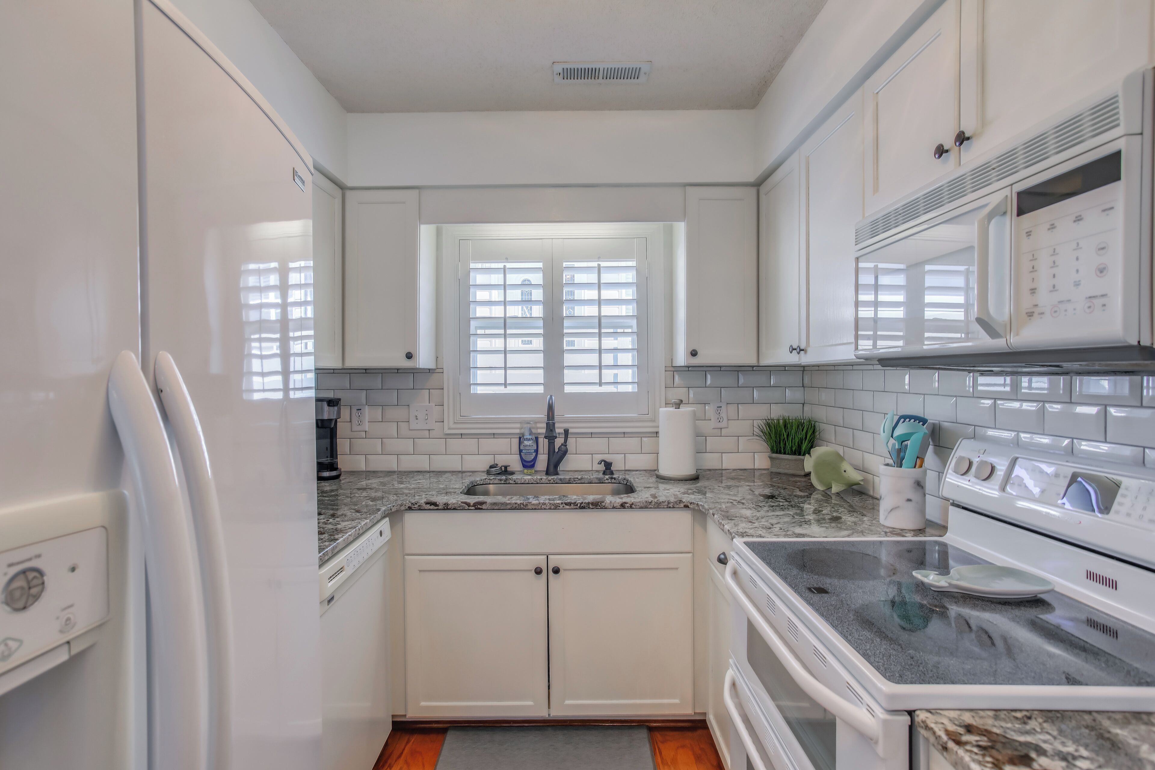 A modern kitchen with white cabinets, a granite countertop, a built-in oven, and a microwave.