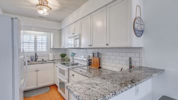 A kitchen with white cabinets, a granite countertop, a built-in oven, and a stainless steel range hood.