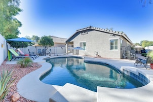 A swimming pool with a curved edge, surrounded by a concrete deck and a small garden area with rocks and plants.