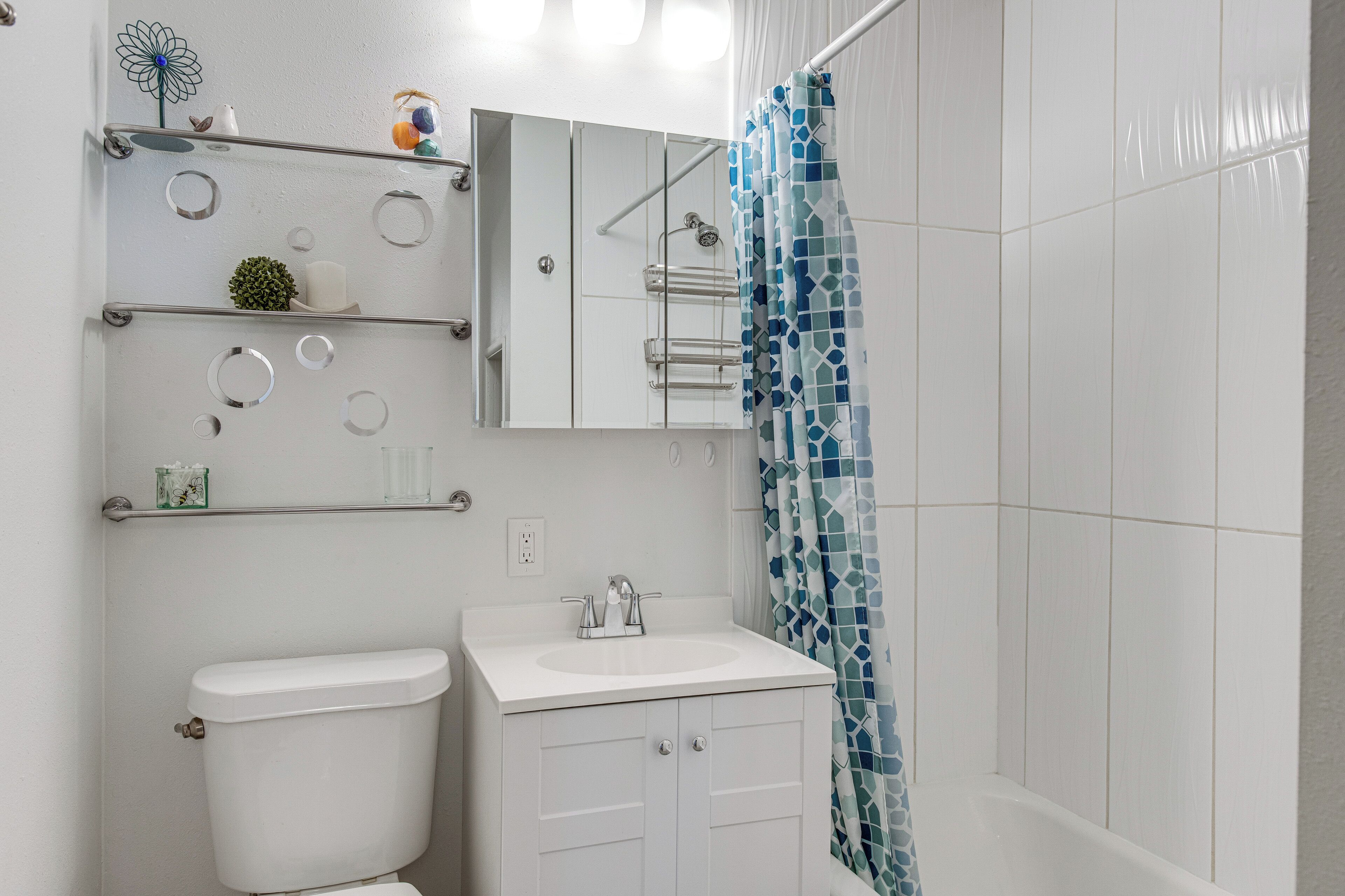 A bathroom with a toilet, sink, mirror, and shelves with toiletries.