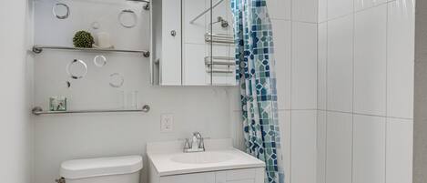 A bathroom with a toilet, sink, mirror, and shelves with toiletries.