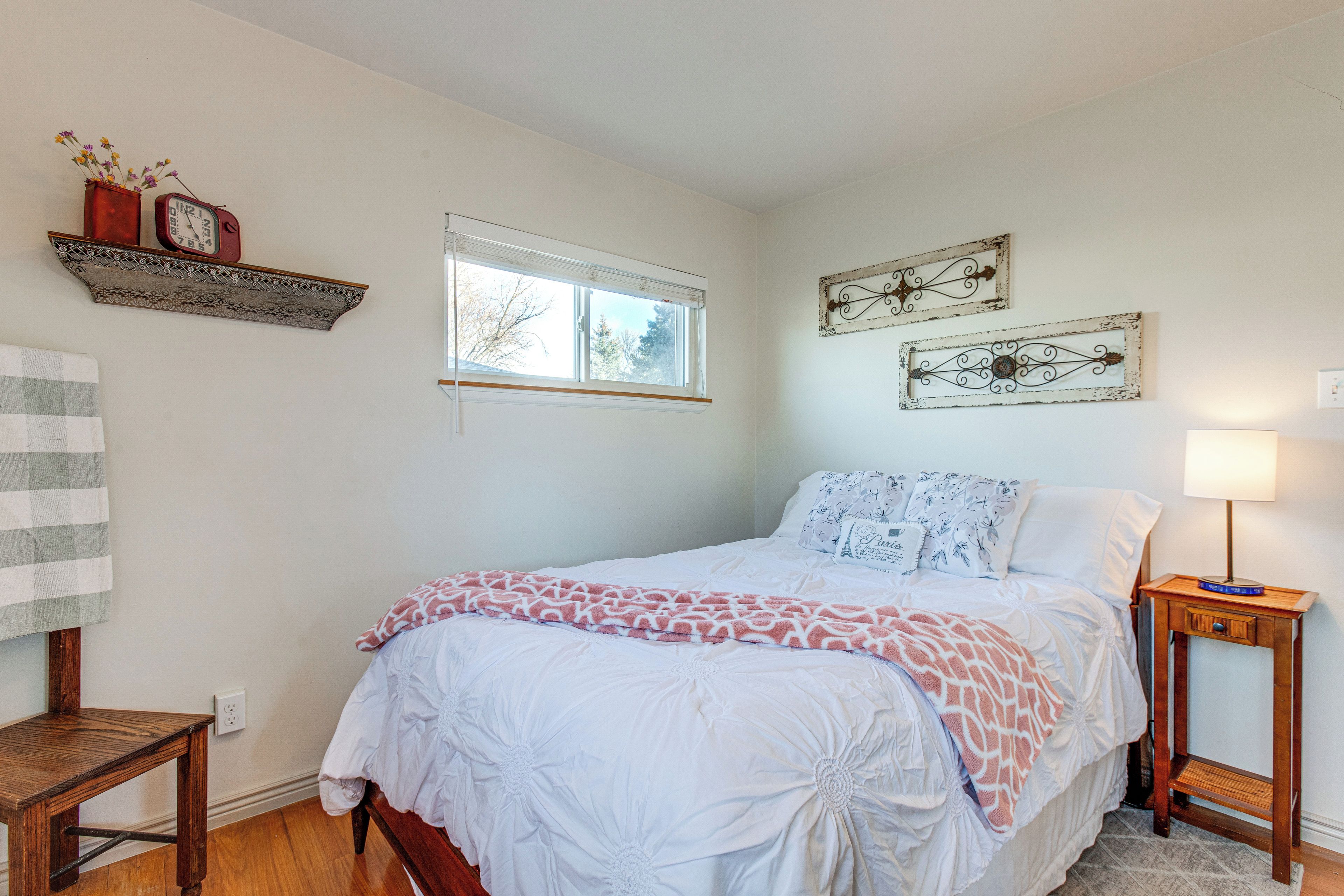 A bedroom with a bed, a nightstand, a window, and decorative wall art.