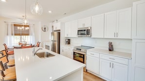 A modern kitchen with white cabinetry, stainless steel appliances, and a central island with a sink. - Charming Charlotte Townhome: 6 Mi to Downtown! (Charlotte)