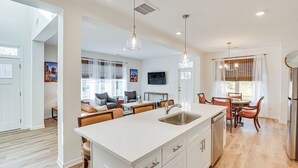 A modern kitchen with a central island, white cabinetry, and a dining area with wicker chairs and a table. - Charming Charlotte Townhome: 6 Mi to Downtown! (Charlotte)