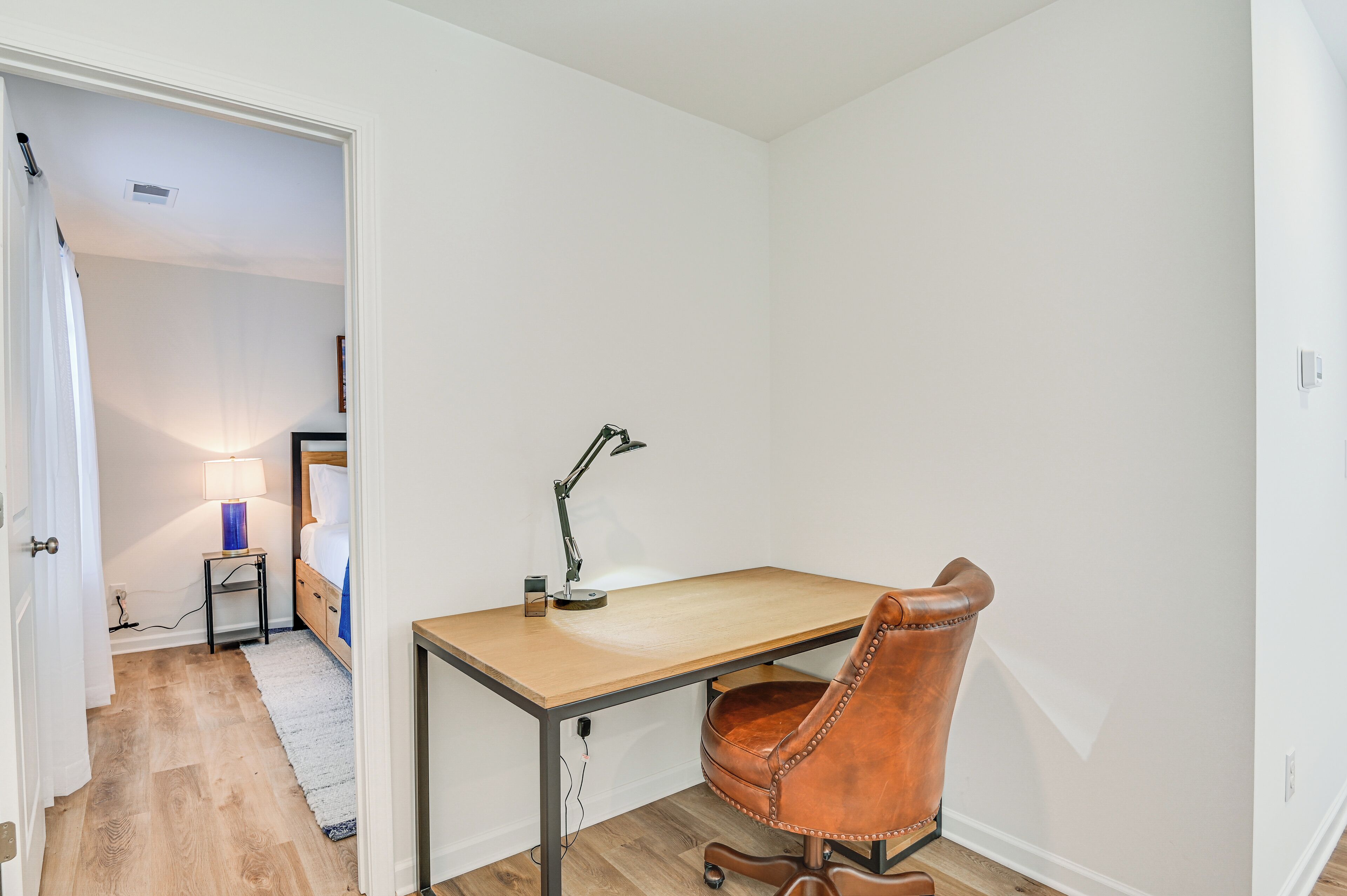Une petite pièce bien éclairée, avec un bureau en bois, un fauteuil en cuir et une lampe.