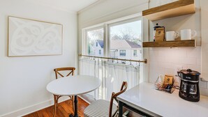 A modern kitchen with a white table, wooden chairs, a coffee maker, and a window with a view of houses. - 2 Mi to Tyler Rose Garden: Vibrant Apartment! (Tyler)