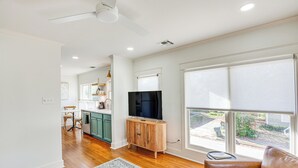 A spacious living room with hardwood floors, a large window with blinds, a ceiling fan, and a flat-screen TV on a wooden cabinet. - 2 Mi to Tyler Rose Garden: Vibrant Apartment! (Tyler)