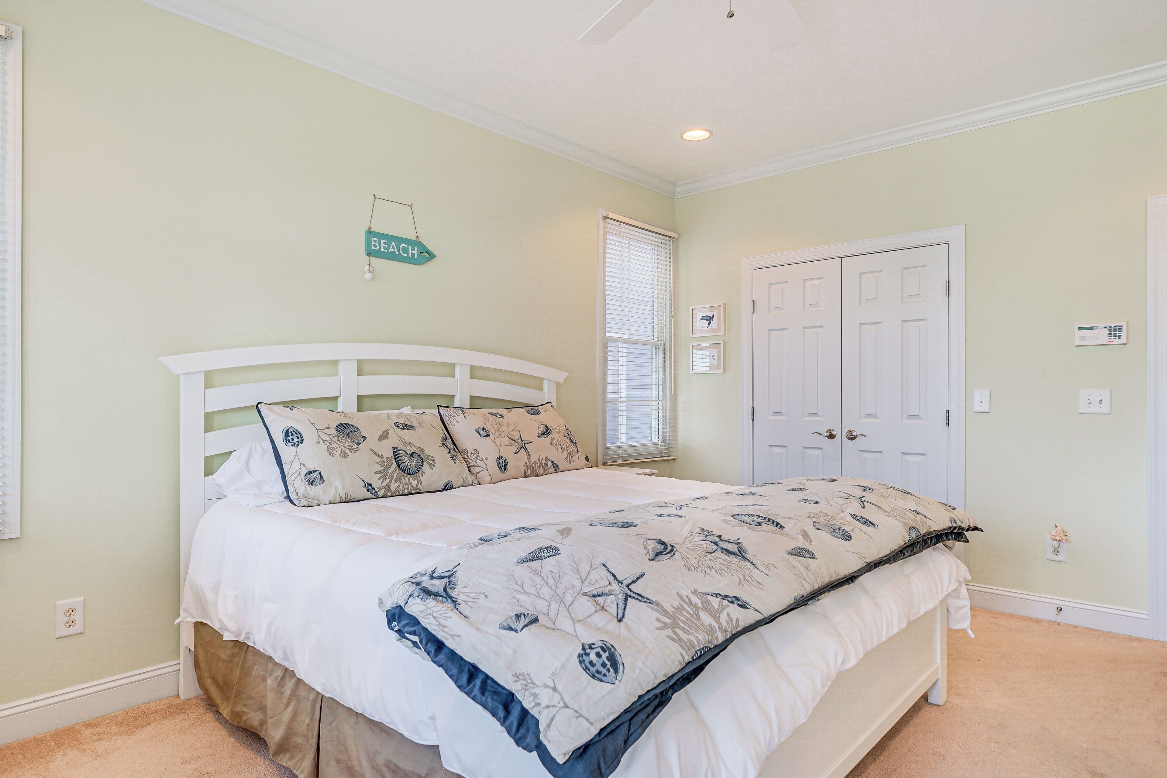 A bedroom with a bed, a door, a thermostat, and a window with blinds.