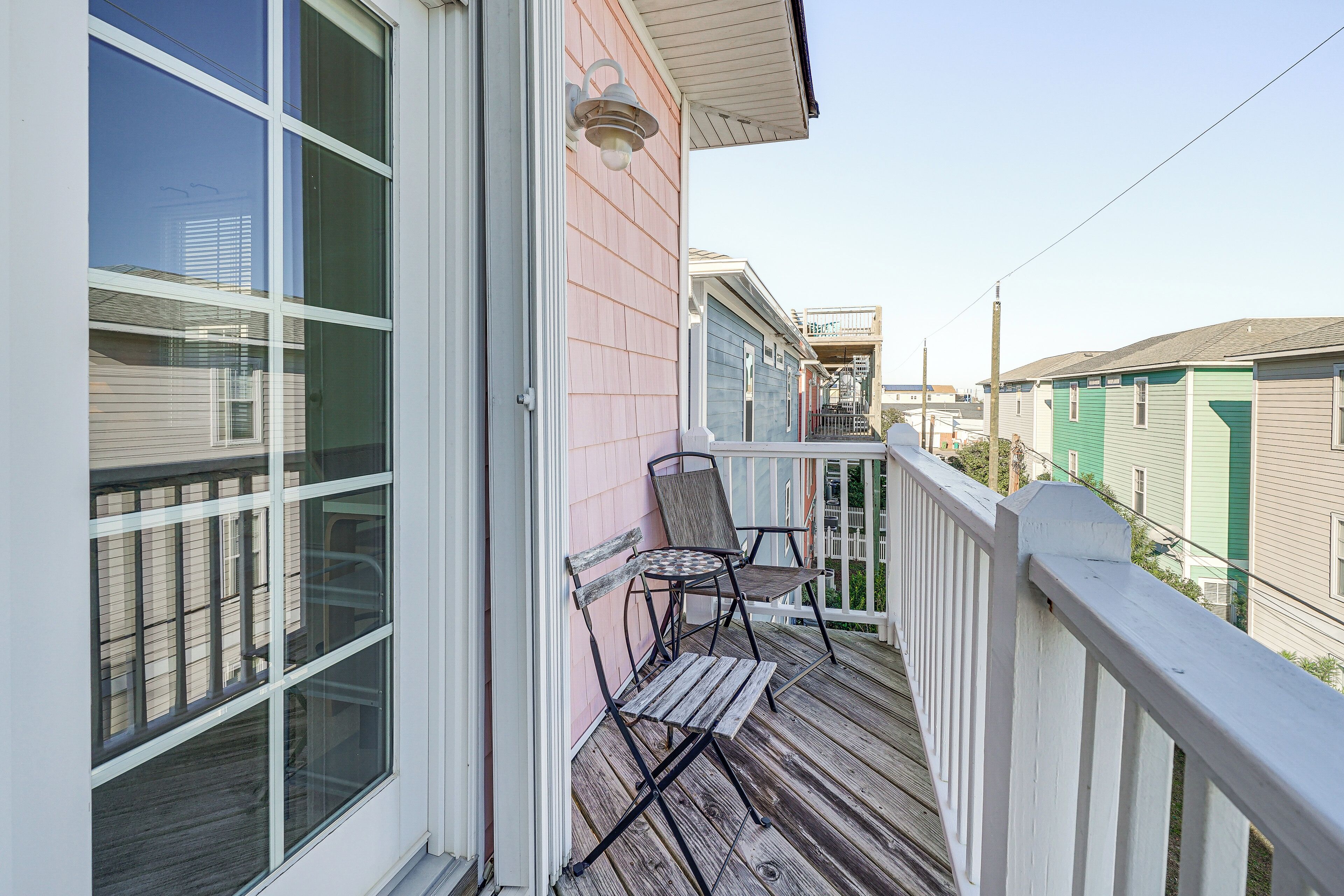 A wooden deck with two chairs and a table, a white railing, and a pink building facade.