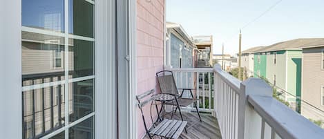 A wooden deck with two chairs and a table, a white railing, and a pink building facade.