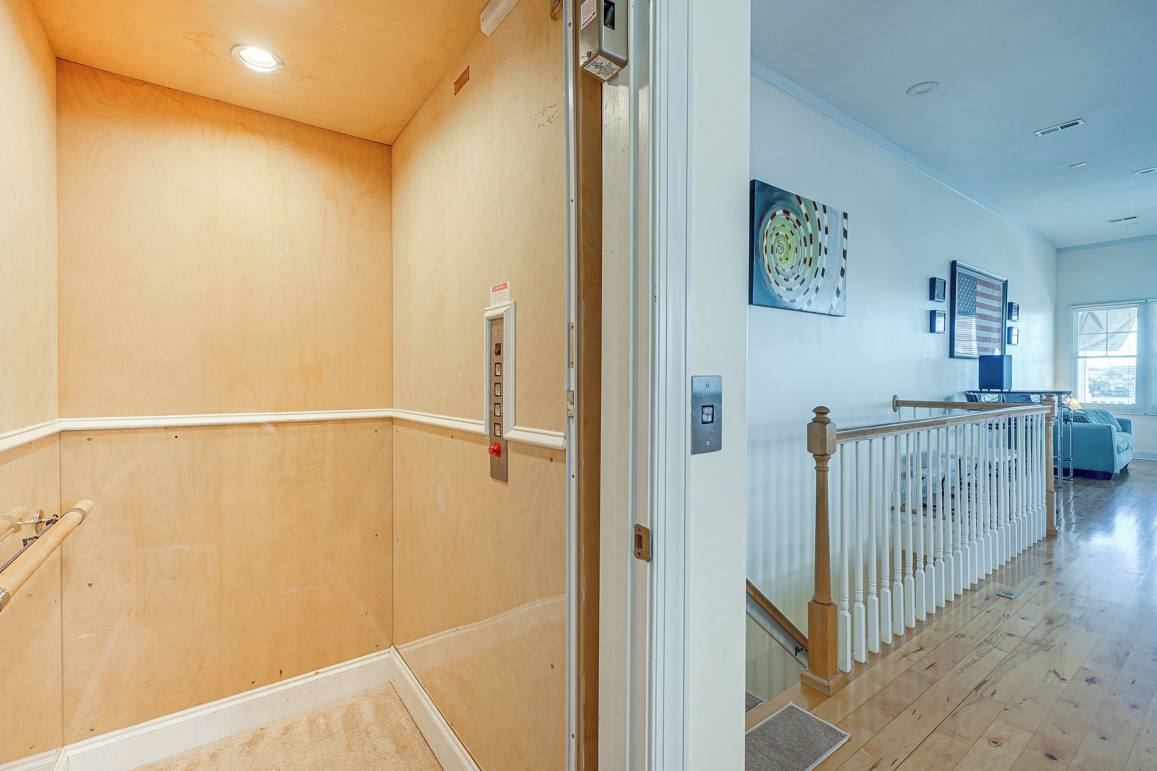 Un couloir aux murs en bois, une rambarde blanche et une porte dotée d’un panneau de commande.