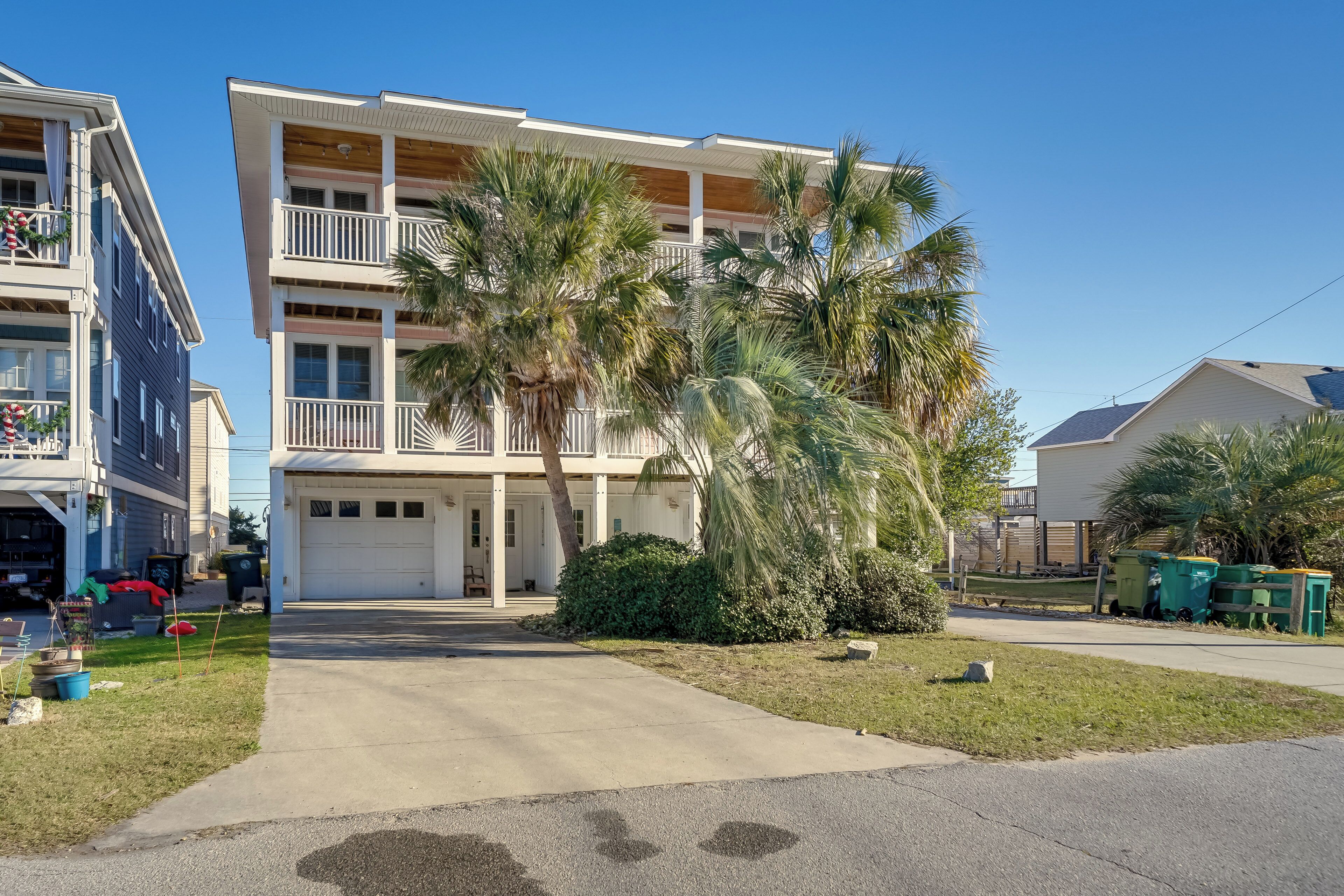 A multi-story residential building with a garage, palm trees, and a well-maintained lawn.