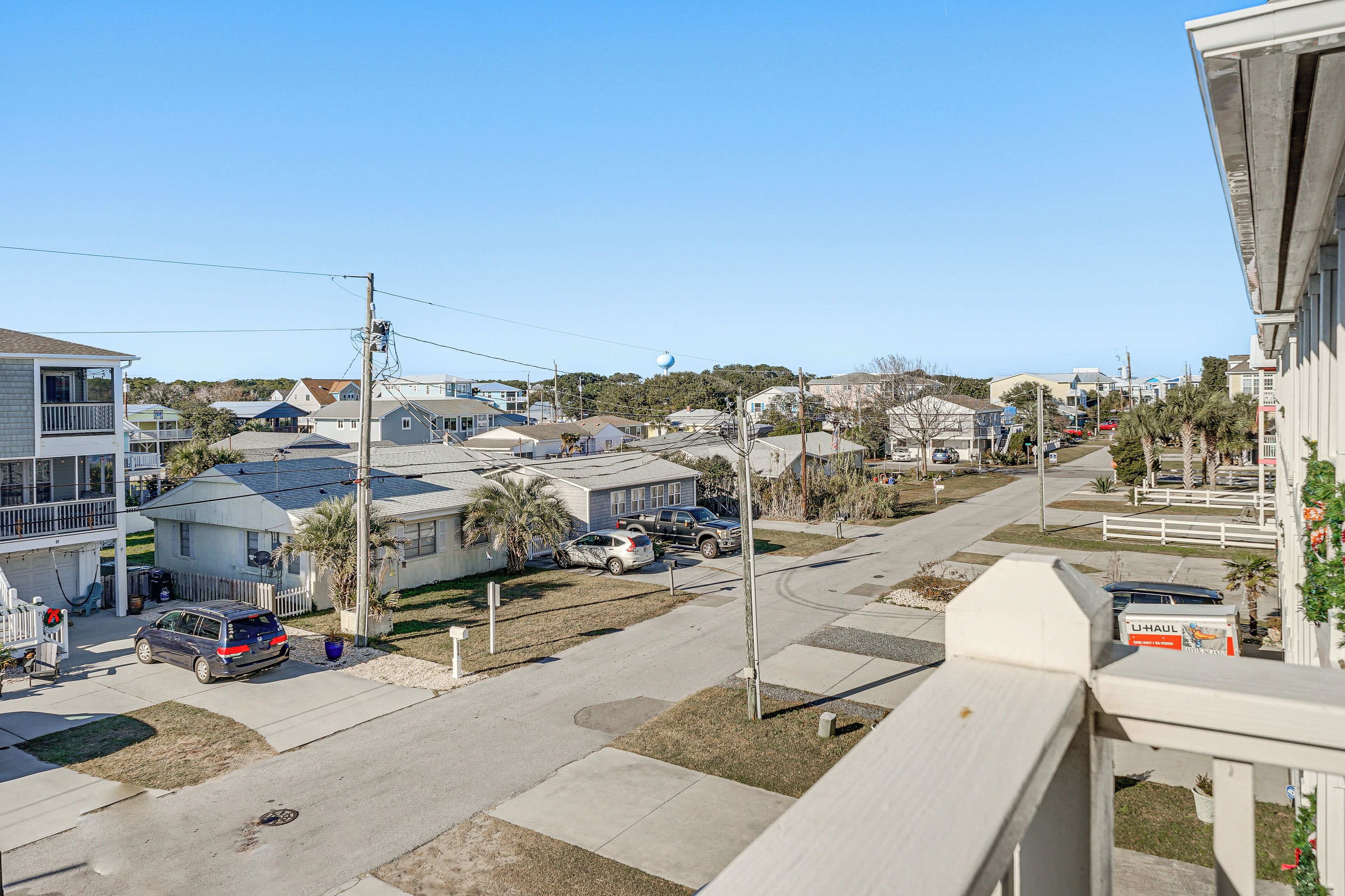 A residential street with houses, parked cars, and a clear sky.