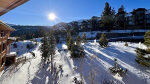 A snow-covered landscape with a view of a multi-story building with balconies, surrounded by trees and mountains in the background. - Ski-in/Ski-out with views at Sunstone (Mammoth Lakes)