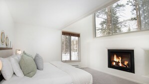 A bedroom with a bed, a fireplace, a window with a view of trees, and a wall-mounted shelf with decorative items. - Private East Vail Home on Bus Rte, 5187GC (Vail)