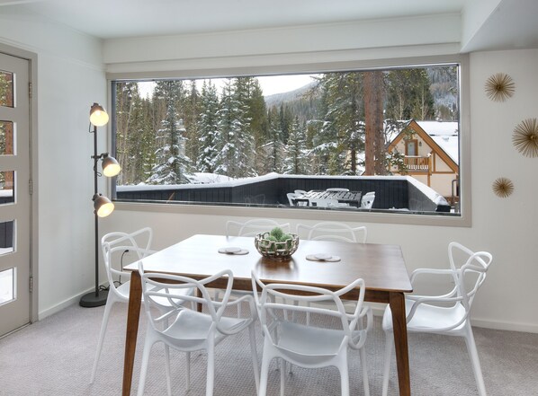 Ein Essbereich mit großem Fenster, weißen Stühlen, einem Holztisch und einer Stehlampe.